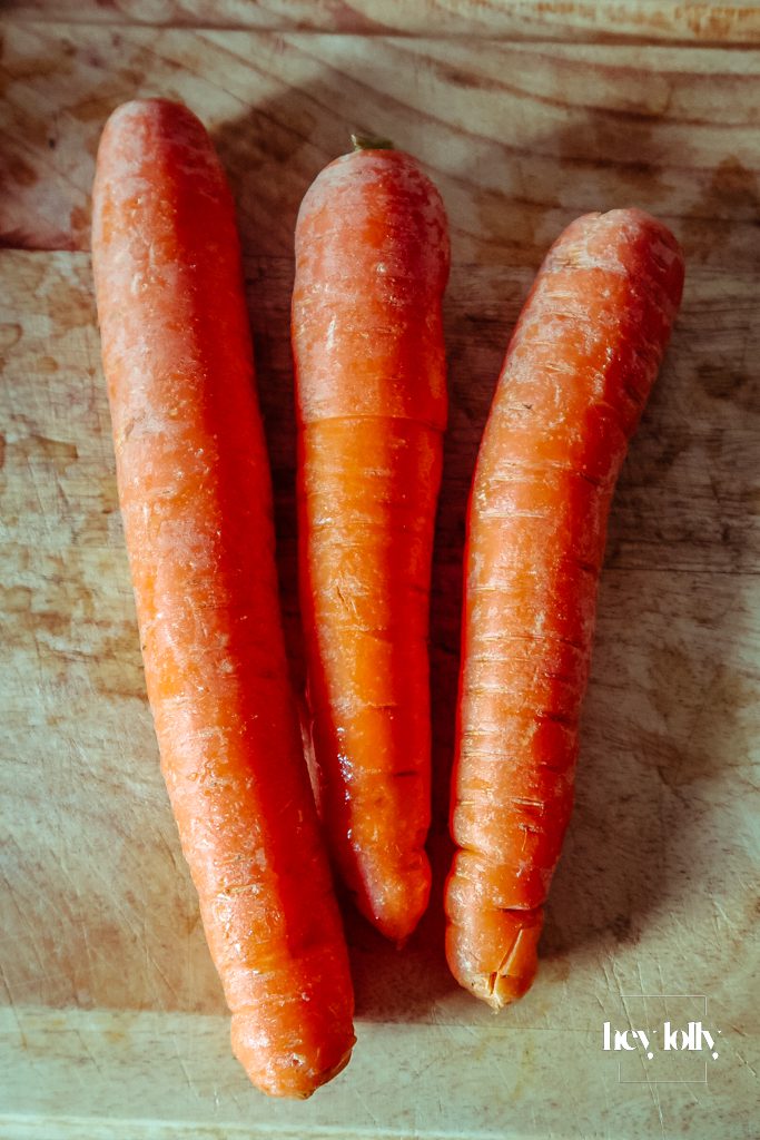 Unprepared ingredients for pearl barley stew on a wooden board: pearl barley, smoky sausages, carrots, onions, garlic, greens, white beans and fresh herbs