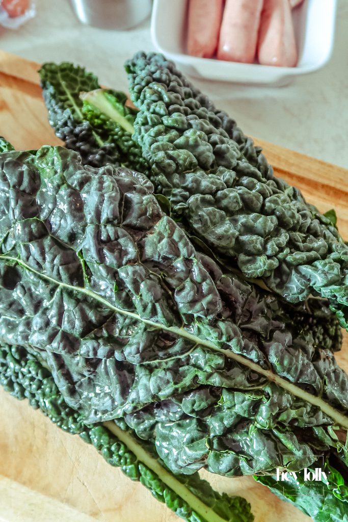 Unprepared ingredients for pearl barley stew on a wooden board: pearl barley, smoky sausages, carrots, onions, garlic, greens, white beans and fresh herbs