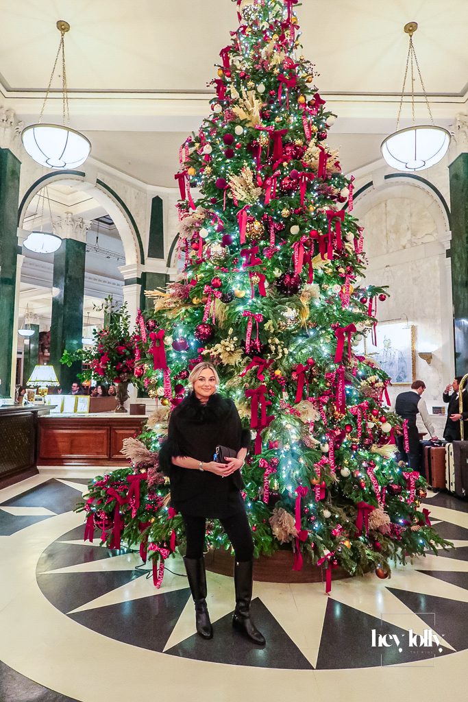 Person photographed beside the main Christmas tree in The Ned London hotel hall
