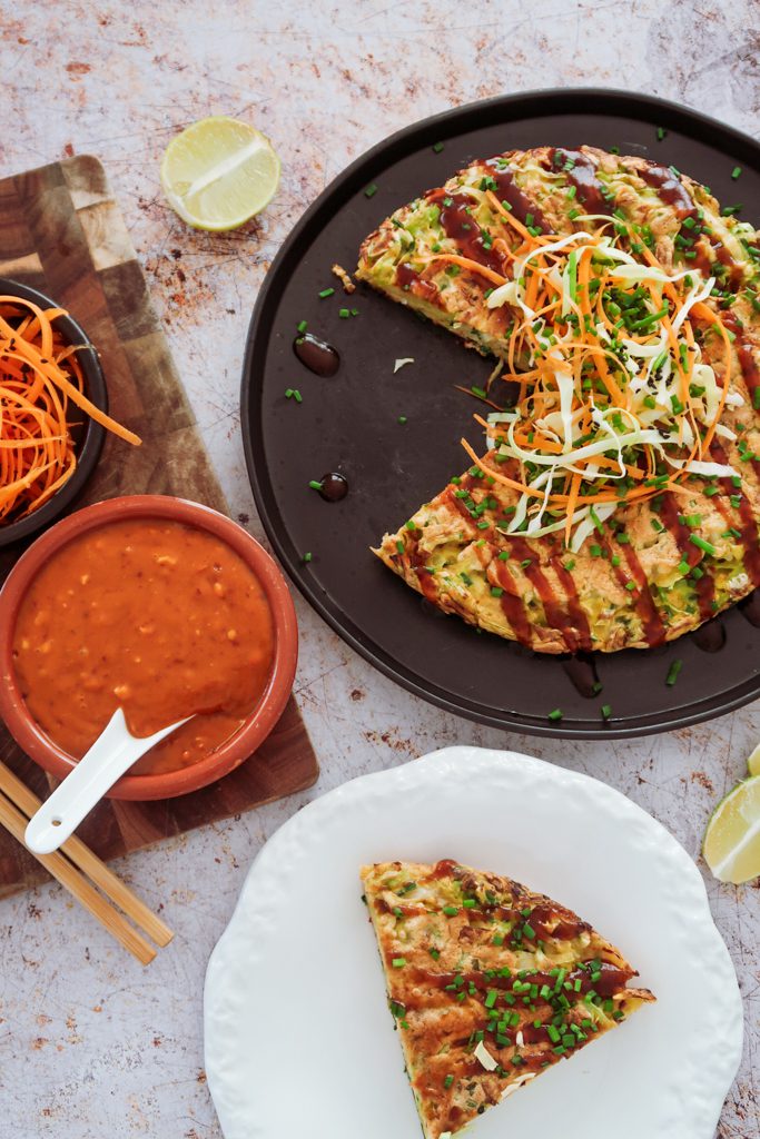 Okonomiyaki pancakes with gochujang and peanut sauce on a ceramic plate with spring onions and sesame seeds