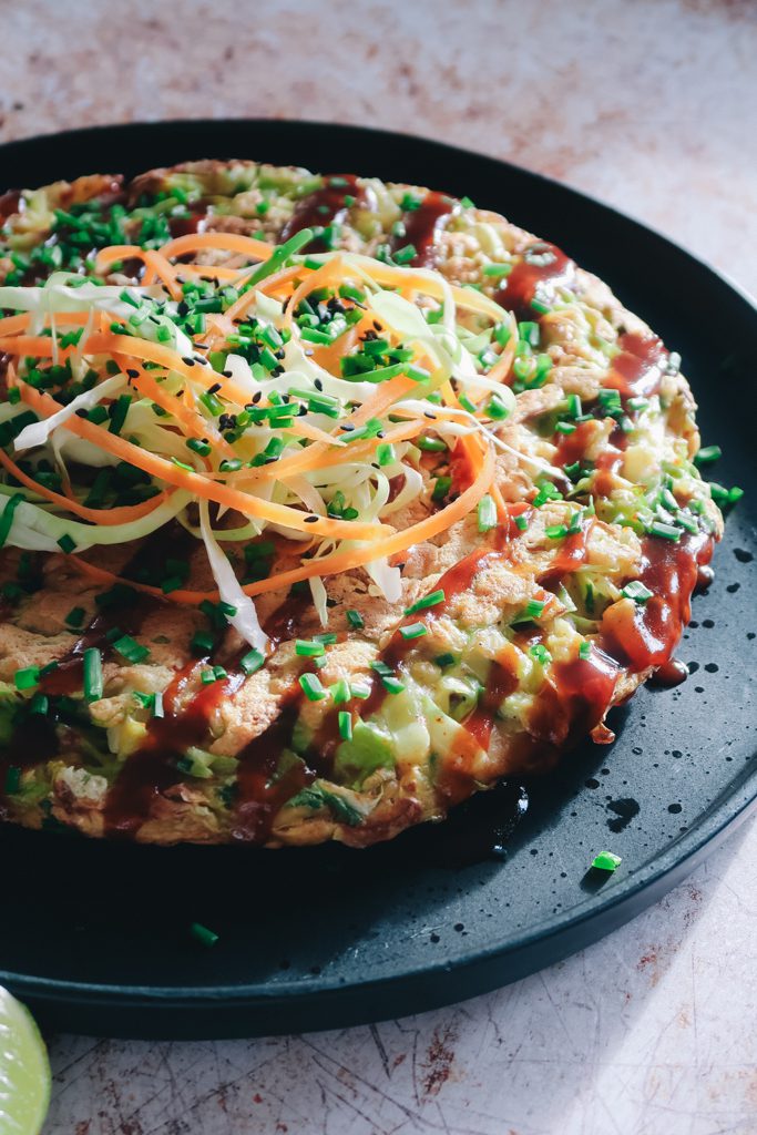 close-up of okonomiyaki pancake with gochujang showing crisp edges, cabbage interior and sauce drizzles