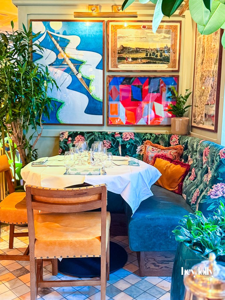Interior of The Ivy Nottingham dining room with brass tables, velvet seating and artwork creating an elegant restaurant setting