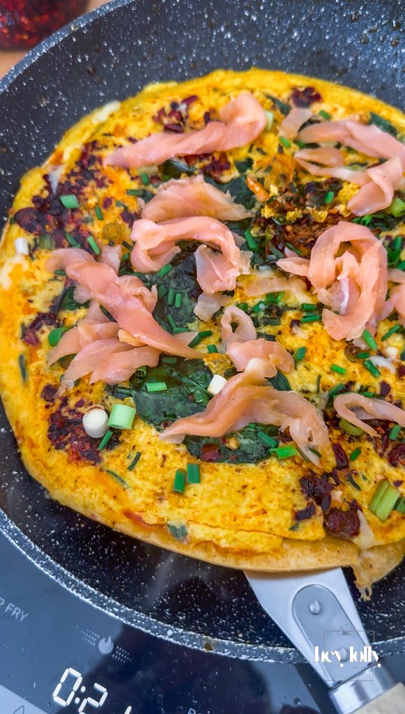 Egg and cream mixture cooking in pan with greens for smoked salmon breakfast quesadilla